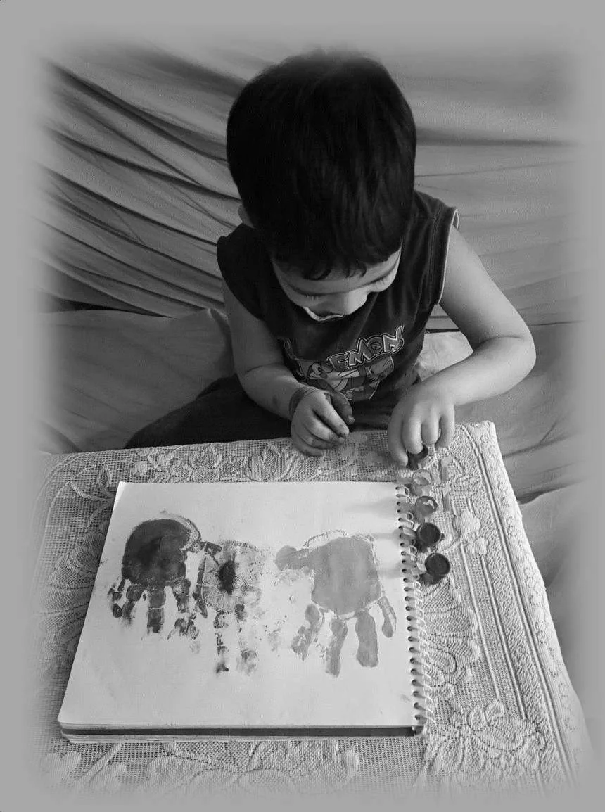A small boy beside a sketchbook of painted handprints, opening pots of paint