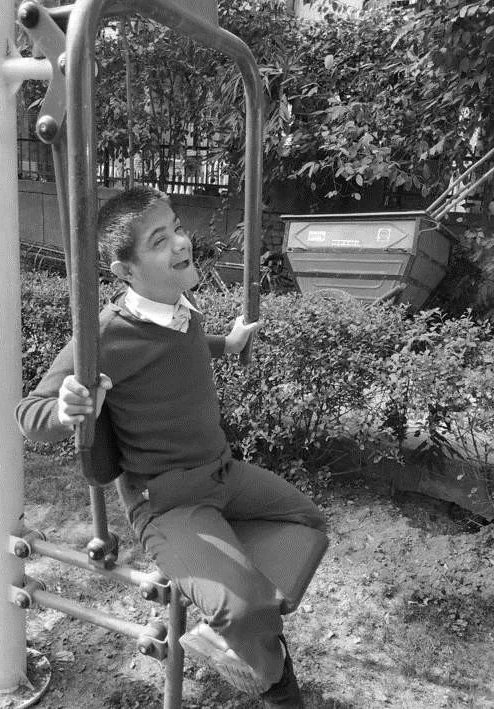A boy sitting on outdoor exercise equipment in a garden