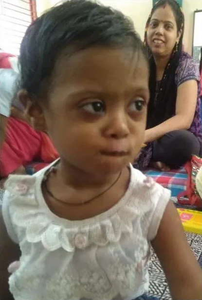 A young girl looking to the side, with a woman sitting behind her