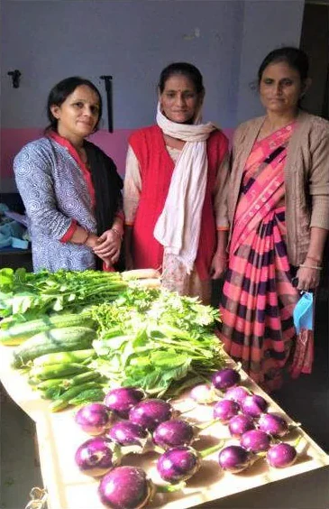 Three women standing behind fresh vegetables from the garden