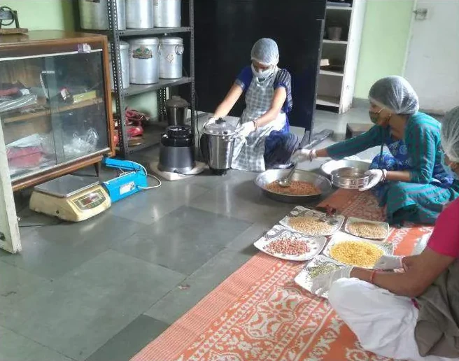Women in hairnets and gloves sorting grains and nuts in a kitchen